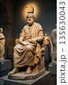 Ancient marble statue of philosopher seated in museum with other sculptures in background 135630043