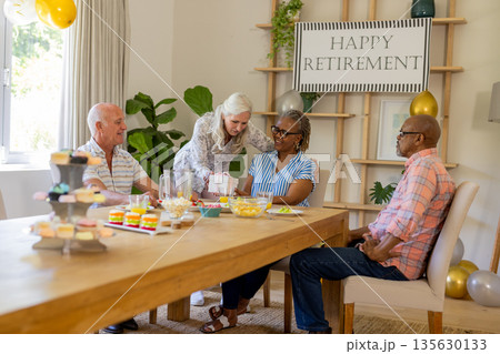 Senior friends celebrating retirement with snacks and laughter at home gathering 135630133
