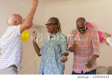 Senior friends dancing joyfully at home, celebrating with colorful balloons Senior friends dancing joyfully at home, celebrating with colorful balloons 135630143