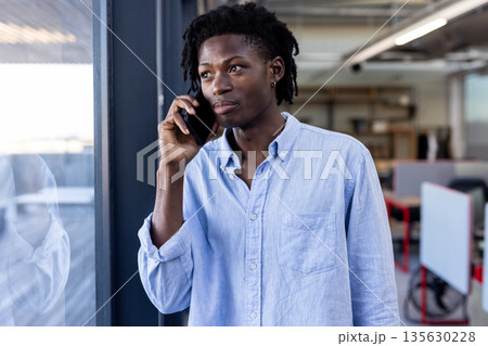 Talking on smartphone, professional standing by office window, looking thoughtful Talking on smartphone, professional standing by office window, looking thoughtful 135630228