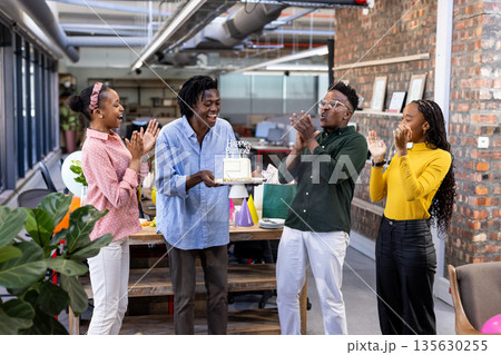 Celebrating birthday with cake, African American colleagues smiling joyfully in modern office 135630255