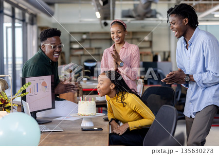 Colleagues celebrating birthday in office as woman blows out candles on cake Colleagues celebrating birthday in office as woman blows out candles on cake 135630278