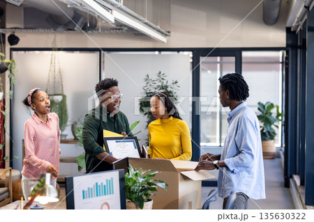 Unpacking boxes and discussing ideas, African American colleagues collaborating in office 135630322
