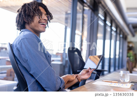 Smiling man holding tablet in modern office, enjoying creative business meeting Smiling man holding tablet in modern office, enjoying creative business meeting 135630338