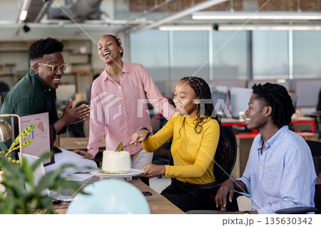Celebrating birthday with cake, African American colleagues smiling in modern office 135630342