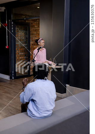 Woman presenting at podium while audience member clapping in modern office Woman presenting at podium while audience member clapping in modern office 135630376