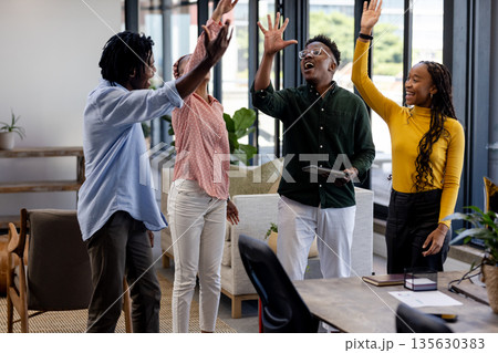 Diverse team celebrating success with high fives in modern office space Diverse team celebrating success with high fives in modern office space 135630383