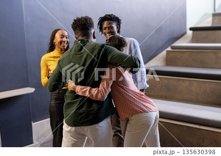 African American colleagues hugging and laughing together in modern office stairwell African American colleagues hugging and laughing together in modern office stairwell 135630398