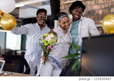 Congratulating coworker with flowers, African American colleagues celebrating success in office Congratulating coworker with flowers, African American colleagues celebrating success in office 135630407