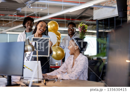 Celebrating promotion, African American colleagues with balloons and sign in office 135630415