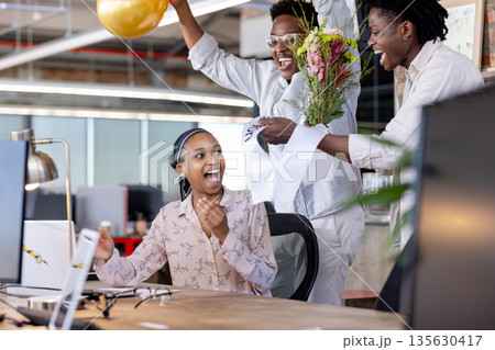 Surprising woman with flowers, African American colleagues celebrating success at office Surprising woman with flowers, African American colleagues celebrating success at office 135630417