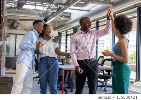 Colleagues celebrating success with high fives and laughter in modern office 135630421
