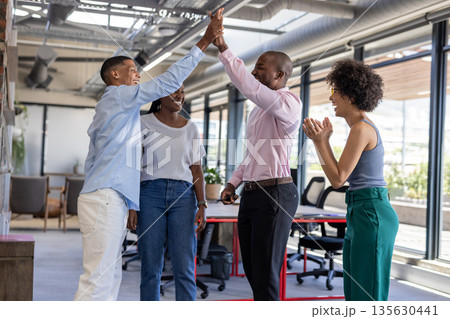 Colleagues in office celebrating success with high fives and smiles Colleagues in office celebrating success with high fives and smiles 135630441
