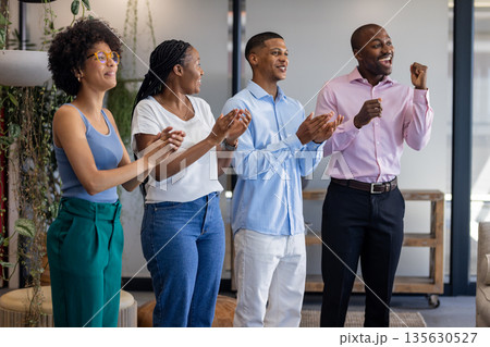 Diverse team celebrating success in office, clapping and smiling with excitement 135630527