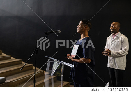 Receiving award on stage, African American man applauded by audience in auditorium 135630586