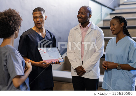 Discussing award certificate, medical professionals smiling and engaged in hospital hallway 135630590