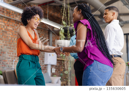 Colleagues in office laughing and shaking hands, enjoying team bonding moment 135630605