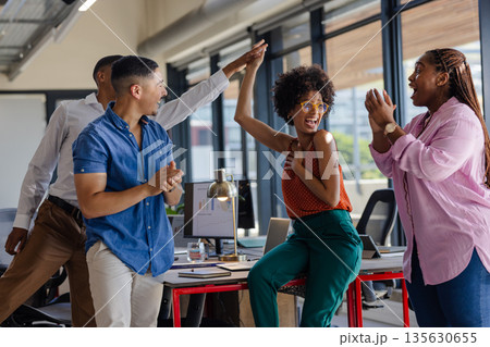 Colleagues celebrating success with high fives in modern office setting 135630655