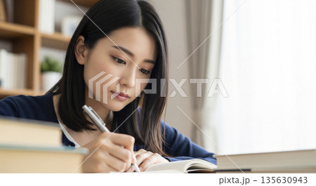 部屋で真剣な表情でノートに書き込み勉強する日本人女性 部屋で真剣な表情でノートに書き込み勉強する日本人女性 135630943