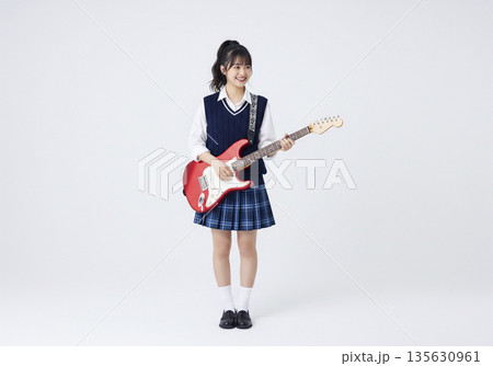 白い背景で赤いエレキギターを抱えて遠くを見つめる笑顔の日本人女子高生 135630961