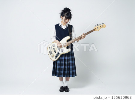 グレーの背景で真剣な表情でベースの指板を見つめて演奏する可愛い女性ベーシスト グレーの背景で真剣な表情でベースの指板を見つめて演奏する可愛い女性ベーシスト 135630968