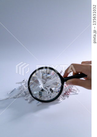 虫眼鏡でシュレッダーの屑を調べる手元 135631032