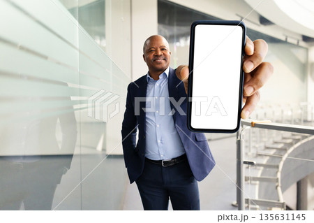 Black mature businessman holding smartphone with blank screen toward camera Black mature businessman holding smartphone with blank screen toward camera 135631145