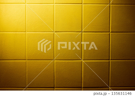 Yellow padded wall panel texture with square grid pattern, soft fabric surface, subtle depth and warm studio lighting. Copy space 135631146