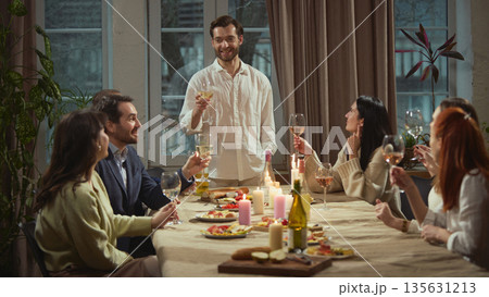 Man standing making toast during group dinner. Man standing making toast during group dinner. 135631213