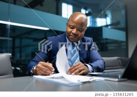 Black mature businessman signing documents at desk in modern office Black mature businessman signing documents at desk in modern office 135631265