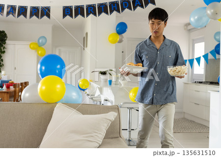 Young man carrying snacks at home, preparing for birthday celebration Young man carrying snacks at home, preparing for birthday celebration 135631510