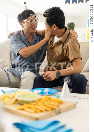 Friends celebrating baby shower, laughing and enjoying snacks on living room couch 135631511