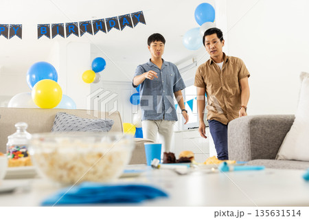Two men preparing birthday party decorations with balloons and snacks at home Two men preparing birthday party decorations with balloons and snacks at home 135631514