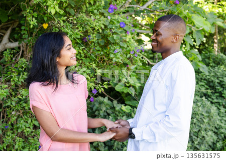 Couple holding hands and smiling at each other in lush garden setting 135631575