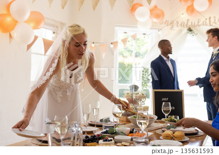 Bride arranging table setting at wedding reception with guests enjoying celebration Bride arranging table setting at wedding reception with guests enjoying celebration 135631593