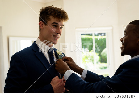 Groom smiling while friend adjusts boutonniere, preparing for wedding ceremony 135631597