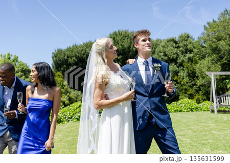Celebrating outdoors, bride and groom holding champagne glasses with smiling friends Celebrating outdoors, bride and groom holding champagne glasses with smiling friends 135631599