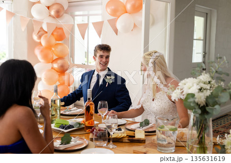 Bride and groom smiling at table with friends during wedding celebration Bride and groom smiling at table with friends during wedding celebration 135631619