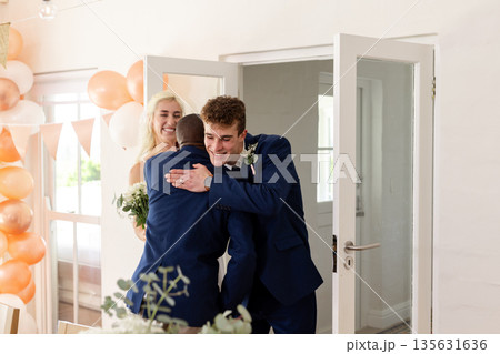 Groom hugging friend at wedding reception, both smiling joyfully in celebration Groom hugging friend at wedding reception, both smiling joyfully in celebration 135631636