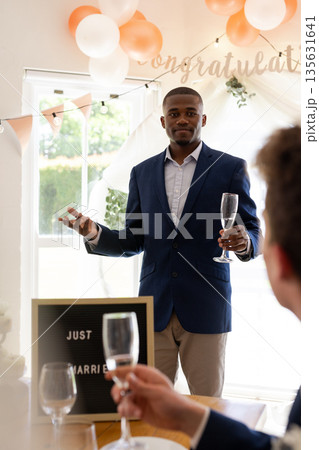 Groom giving heartfelt toast holding champagne glass at wedding celebration indoors 135631641