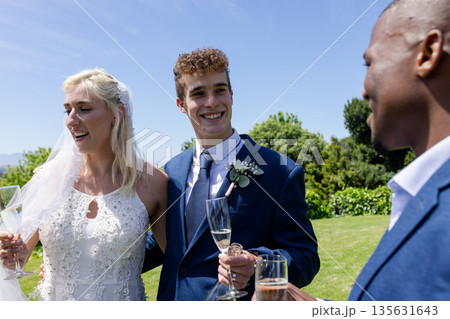 Bride and groom celebrating outdoors with friends, enjoying champagne and laughter 135631643