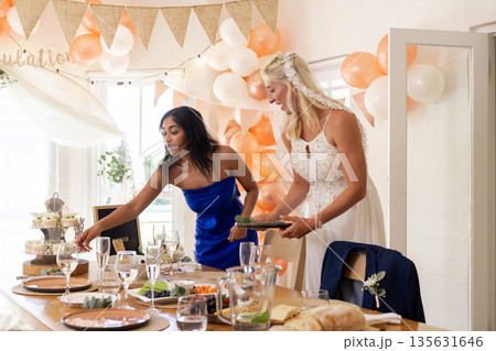 Bride and friend arranging table settings at festive wedding reception Bride and friend arranging table settings at festive wedding reception 135631646
