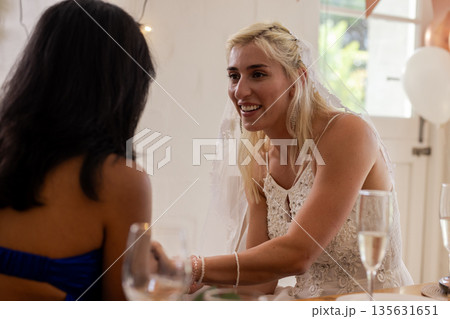 Bride in white dress joyfully chatting with guest at wedding reception Bride in white dress joyfully chatting with guest at wedding reception 135631651