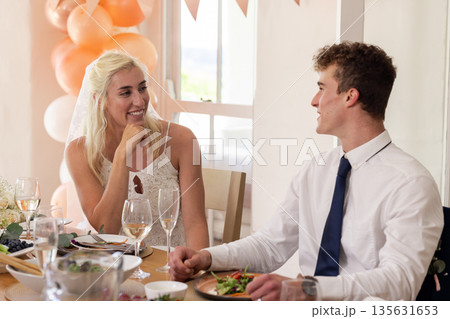 Bride and groom in joyful conversation during wedding reception, sharing smiles 135631653
