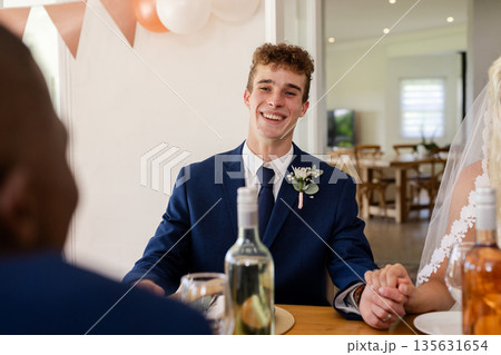 Groom in blue suit smiling while holding hands during wedding celebration Groom in blue suit smiling while holding hands during wedding celebration 135631654