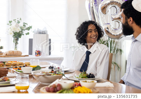 Smiling boy in white shirt enjoying festive meal with family at dining table 135631735