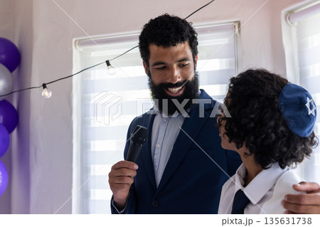 Man holding microphone smiling at boy wearing kippah during bar mitzvah Man holding microphone smiling at boy wearing kippah during bar mitzvah 135631738