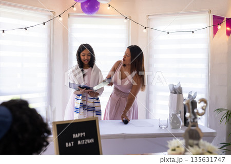 Young girl reading from book during Bat Mitzvah celebration with supportive woman Young girl reading from book during Bat Mitzvah celebration with supportive woman 135631747
