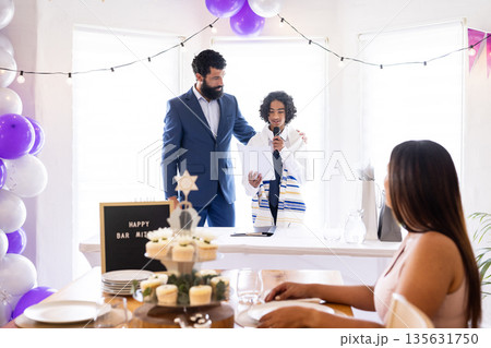 Celebrating Bar Mitzvah, boy speaking into microphone with family and decorations Celebrating Bar Mitzvah, boy speaking into microphone with family and decorations 135631750