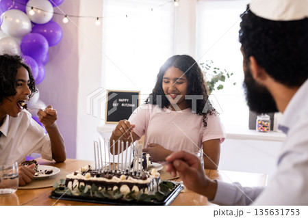 Family celebrating Bat Mitzvah with cake, sharing joyful moments together at home 135631753